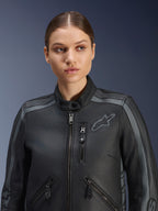 Modelka w kurtce skórzanej Alpinestars Stella Dyno w kolorze Black Tar Gray Dark Gray, motocyklowa kurtka z najwyższej jakości skóry bydlęcej o klasycznym designie, z szarymi akcentami na ramionach i licznymi kieszeniami na zamek, dopasowana do kobiecej sylwetki.