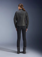 Widok z tyłu kobiety ubranej w skórzaną kurtkę Alpinestars Stella Dyno, czarna z akcentami Haute Red, w zestawieniu z dopasowanymi czarnymi spodniami i czarnymi butami, nowoczesny design skórzanej kurtki motocyklowej typu heritage.