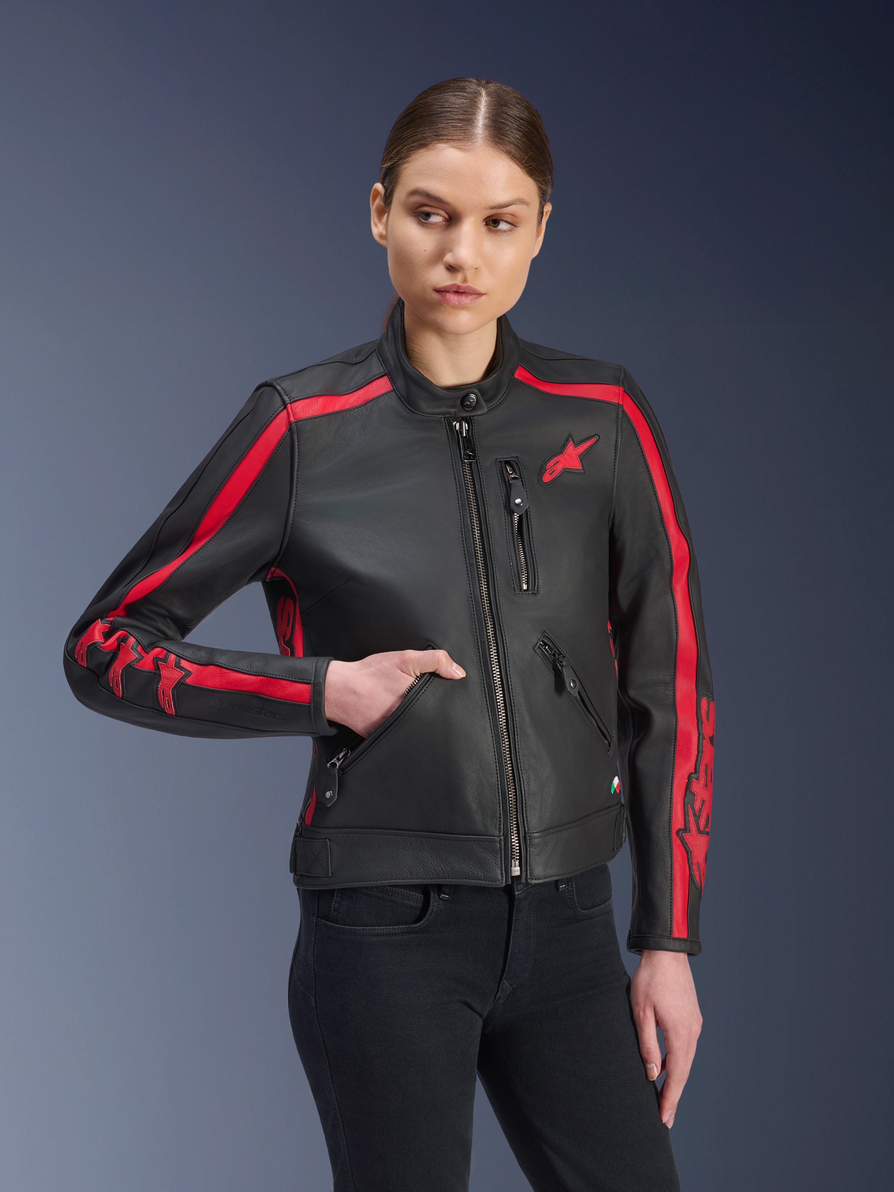 Alpinestars Stella Dyno, damska skórzana kurtka motocyklowa, czarna z czerwonymi pasami wyścigowymi na ramionach i rękawach, prezentowana przez modelkę w czarnych jeansach, wysokiej jakości skóra, design inspirowany stylem heritage do jazdy miejskiej