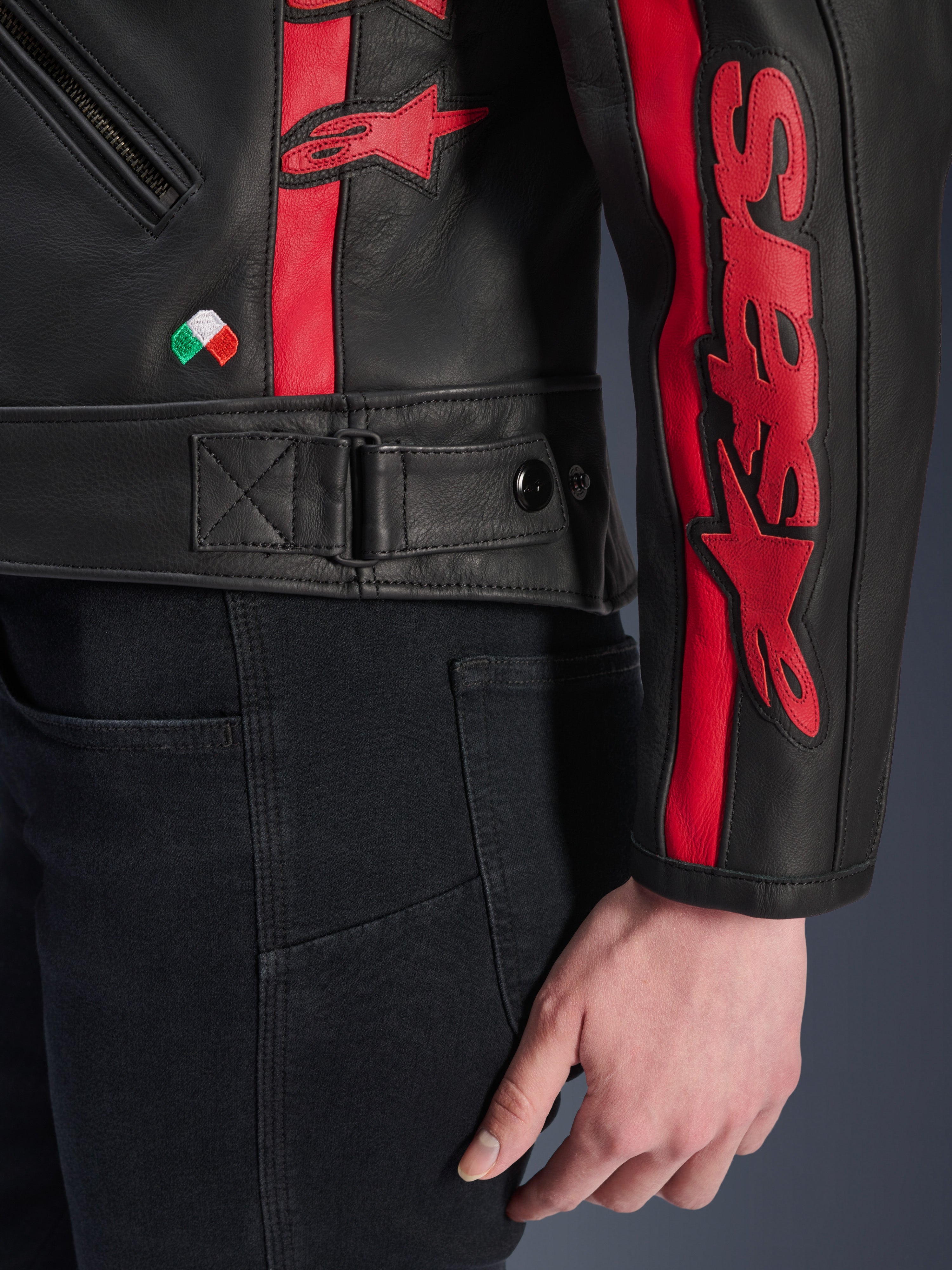 Alpinestars Stella Dyno Leather Jacket, damska skórzana kurtka motocyklowa, Black Haute Red, zbliżenie na talię i rękaw, czerwone paski wyścigowe z brandingiem Alpinestars, regulowany pasek w talii, mały haft z flagą Włoch, konstrukcja z wysokiej jakości skóry bydlęcej