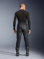Alpinestars Missile V3 Leather Pants, czarne, widok z tyłu na modelu ubranym w czarną koszulkę kompresyjną z długim rękawem i buty wyścigowe, konstrukcja z wysokiej jakości skóry z podwyższonym stanem i strefami elastycznymi, profesjonalna odzież motocyklowa wyścigowa