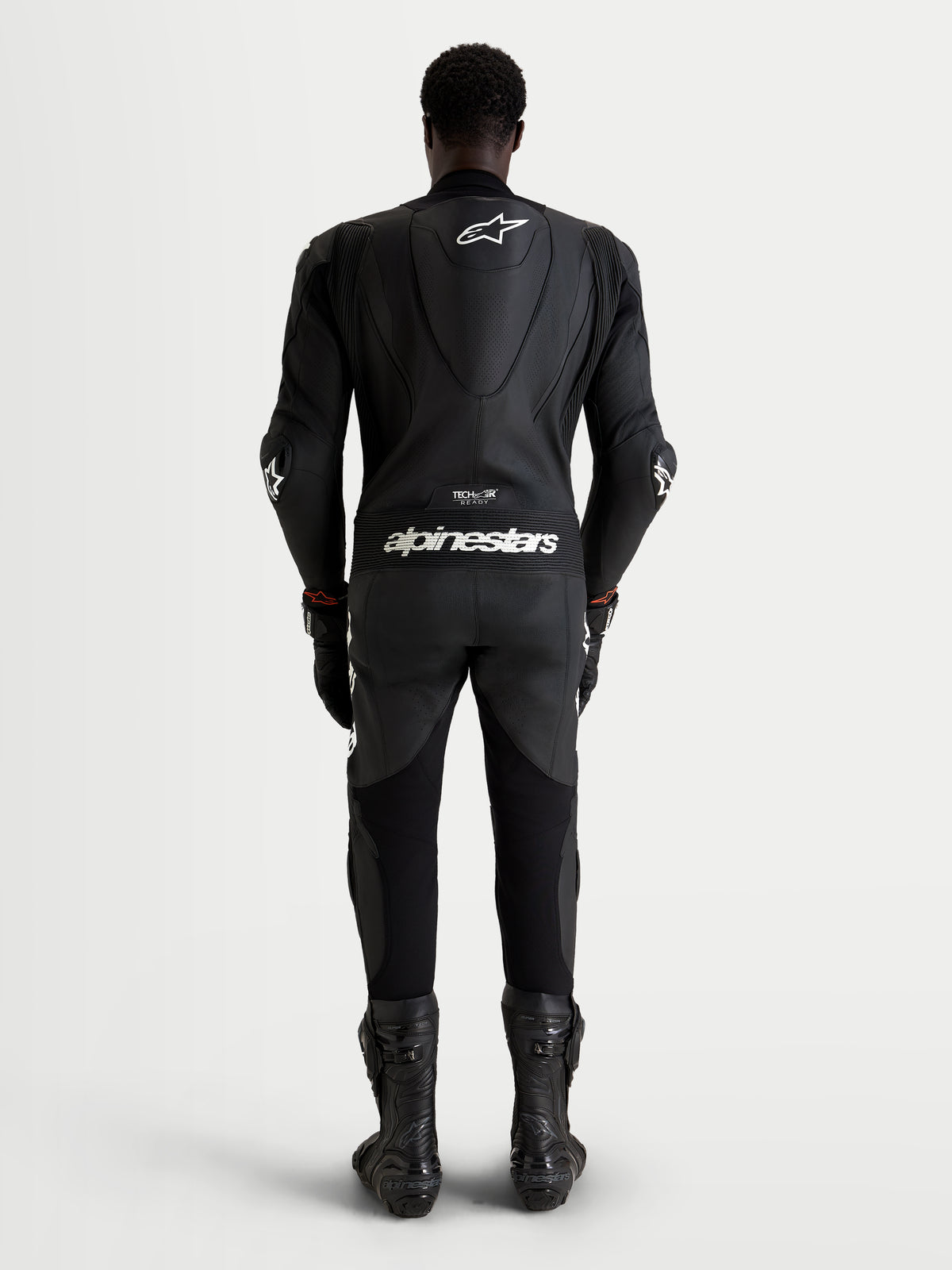 Alpinestars Missile V3 Skórzany Kombinezon 1 Pc, męski kombinezon wyścigowy, czarny skórzany z białymi logo i aerodynamicznym garbem, widok z tyłu na motocyklistę