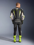Jednoczęściowy kombinezon skórzany Alpinestars GP Tech V5, widok z tyłu, czarno-biało-żółty fluo, aerodynamiczny garb z żółtym logo gwiazdy, białe logo Alpinestars na rękawach i plecach, pasujące neonowe żółte buty wyścigowe, profesjonalny sprzęt motocyklowy na tor