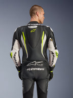 Alpinestars GP Tech V5 One Piece Leather Suit, widok z tyłu na modelu, kolor czarno-biały i żółty fluo, z aerodynamicznym garbem, dużym logo Alpinestars na rękawach i siedzeniu, elastycznymi panelami akordeonowymi oraz logo Tech-Air Ready