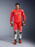 Alpinestars GP Tech V5, jednoczęściowy kombinezon skórzany, profesjonalny kombinezon wyścigowy w kolorach Red Fluo i Bright Red z białymi akcentami, noszony przez motocyklistę z dopasowanymi butami i rękawicami, aerodynamiczny garb, skórzana konstrukcja premium i zaawansowane ochraniacze.
