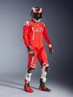 Motocyklista w jednoczęściowym kombinezonie skórzanym Alpinestars GP Tech V5, fluorescencyjna czerwień i jasna czerwień z białymi akcentami, z dopasowanym kaskiem, rękawicami i butami wyścigowymi, profesjonalny sprzęt torowy z perforowaną skórą i sliderami ochronnymi