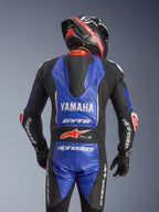 Alpinestars Yamaha GP-R7 One Piece Leather Suit, jednoczęściowy kombinezon skórzany, widok z tyłu, metaliczny niebieski i czarny z białymi i czerwonymi akcentami, wyraźne logo Yamaha i GYTR, aerodynamiczny garb, noszony z dopasowanym kaskiem i rękawicami wyścigowymi, profesjonalny wygląd gotowy na tor