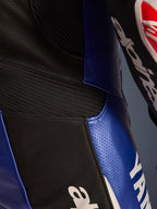 Zbliżenie na detale jednoczęściowego kombinezonu skórzanego Alpinestars Yamaha GP-R7, niebieski metalik i czarny, z perforowanymi panelami skórzanymi zapewniającymi wentylację, czarnymi elastycznymi wstawkami akordeonowymi i wyraźnym białym logo Yamaha, podkreślające konstrukcję z wyścigowej skóry bydlęcej.