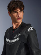 Zbliżenie na mężczyznę ubranego w czarny skórzany kombinezon Alpinestars GP Force V2, z perforowaną konstrukcją skórzaną, logo Alpinestars z napisem „RACING AHEAD” na klatce piersiowej oraz białym logo gwiazdy na ślizgaczach ramion.