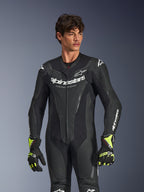 Alpinestars GP Force V2 Leather Suit 1-Piece, czarny, białe logo i oznaczenia Alpinestars, perforowane panele skórzane zapewniające wentylację, noszony przez modela z czarno-neonowożółtymi rękawicami, profesjonalna odzież wyścigowa
