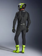 Widok z tyłu motocyklisty w jednoczęściowym skórzanym kombinezonie Alpinestars GP Force V2 w kolorze czarnym, prezentujący aerodynamiczny garb i logo Tech-Air Ready, w zestawie z czarno-neonowożółtym kaskiem oraz jaskrawożółtymi butami wyścigowymi.