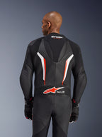 Kombinezon skórzany Alpinestars GP Force V2, jednoczęściowy kombinezon motocyklowy, czarny, biały i czerwony fluo, widok z tyłu górnej części ciała przedstawiający perforowaną skórę i logo Tech-Air Ready, noszony z dopasowanymi czarno-czerwonymi rękawicami