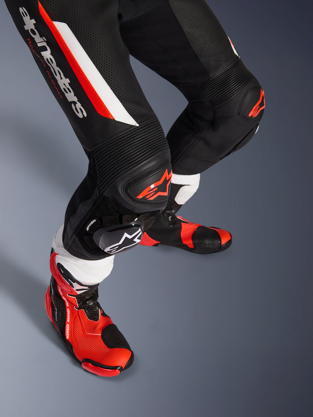 Alpinestars GP Force V2 1-Piece Leather Suit, czarno-biało-czerwony fluo, zbliżenie na dolną część nóg i kolana z ochraniaczami DFS Lite i wymiennymi ślizgaczami, w połączeniu z profesjonalnymi butami wyścigowymi