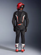 Motocyklista widziany od tyłu w jednoczęściowym skórzanym kombinezonie Alpinestars GP Force V2 w kolorystyce Black White Red Fluo, z aerodynamicznym garbem i oznaczeniem Tech-Air Ready, zestawiony z czerwonym kaskiem wyścigowym oraz biało-czerwonymi butami, profesjonalny design odzieży torowej.
