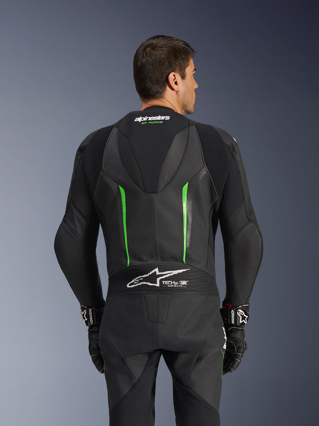 Jednoczęściowy kombinezon skórzany Alpinestars GP Force V2, czarno-zielony, widok z tyłu przedstawiający aerodynamiczny garb, oznaczenie Tech-Air Ready, perforowane strefy skórzane i harmonijkowe panele elastyczne do wyścigów motocyklowych