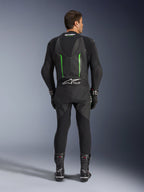 Widok z tyłu jednoczęściowego kombinezonu skórzanego Alpinestars GP Force V2 w kolorze czarno-zielonym, z aerodynamicznym garbem, perforowanymi panelami i logo Tech-Air Ready w dolnej części pleców, noszony z czarnymi rękawicami i butami wyścigowymi.