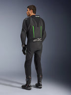 Skórzany kombinezon Alpinestars GP Force V2, jednoczęściowy kombinezon motocyklowy, czarny z zielonymi akcentami, widok z tyłu pokazujący aerodynamiczny garb i białe logo na harmonijkowym panelu elastycznym, w zestawieniu z czarnymi butami i rękawicami wyścigowymi.