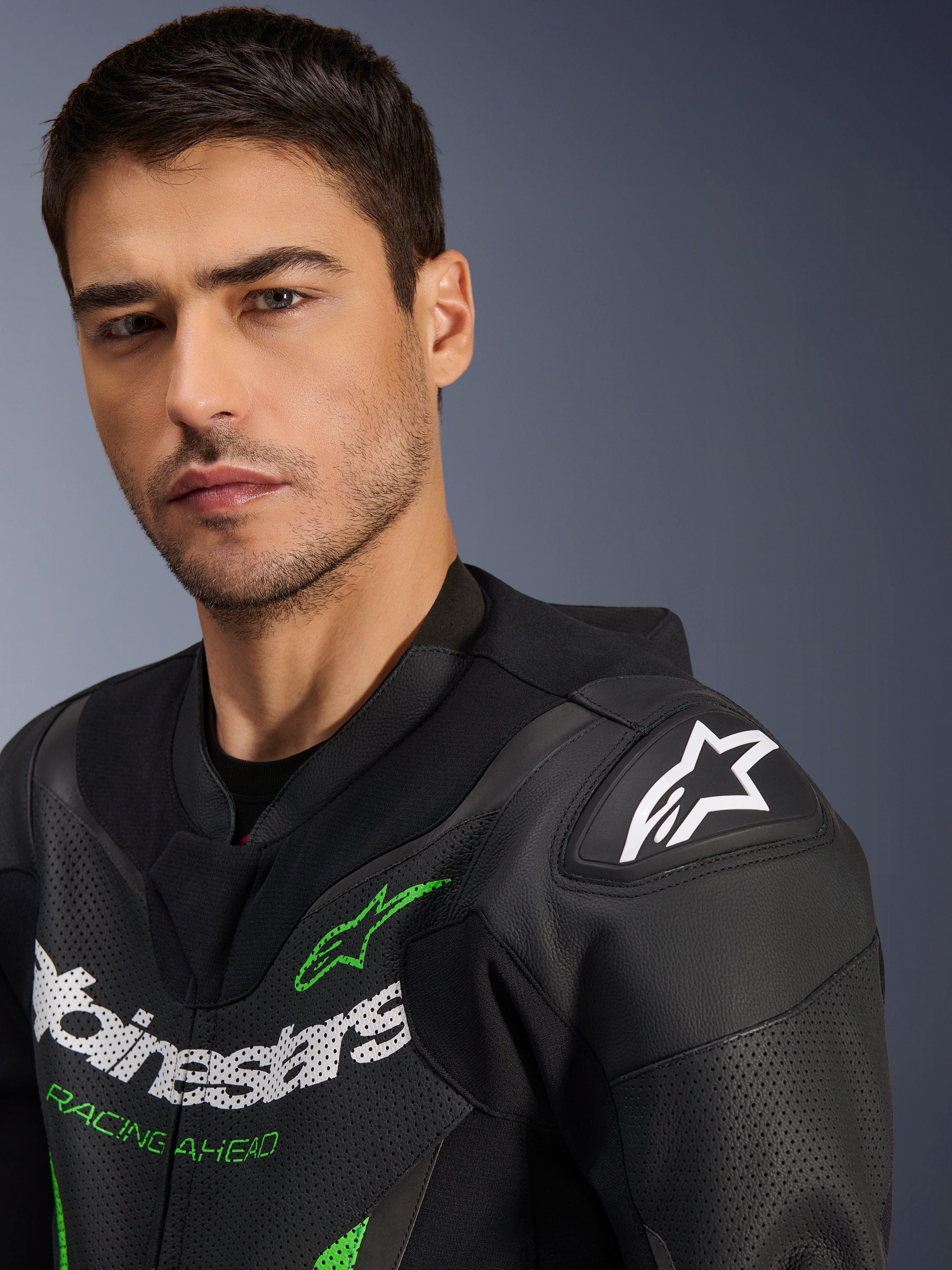 Alpinestars GP Force V2 Leather Suit - 1Piece, czarno-zielony, zbliżenie na modela w motocyklowym kombinezonie wyścigowym, białe i zielone logotypy, perforowane panele skórzane, ochraniacz ramion DFS Lite z białą gwiazdą