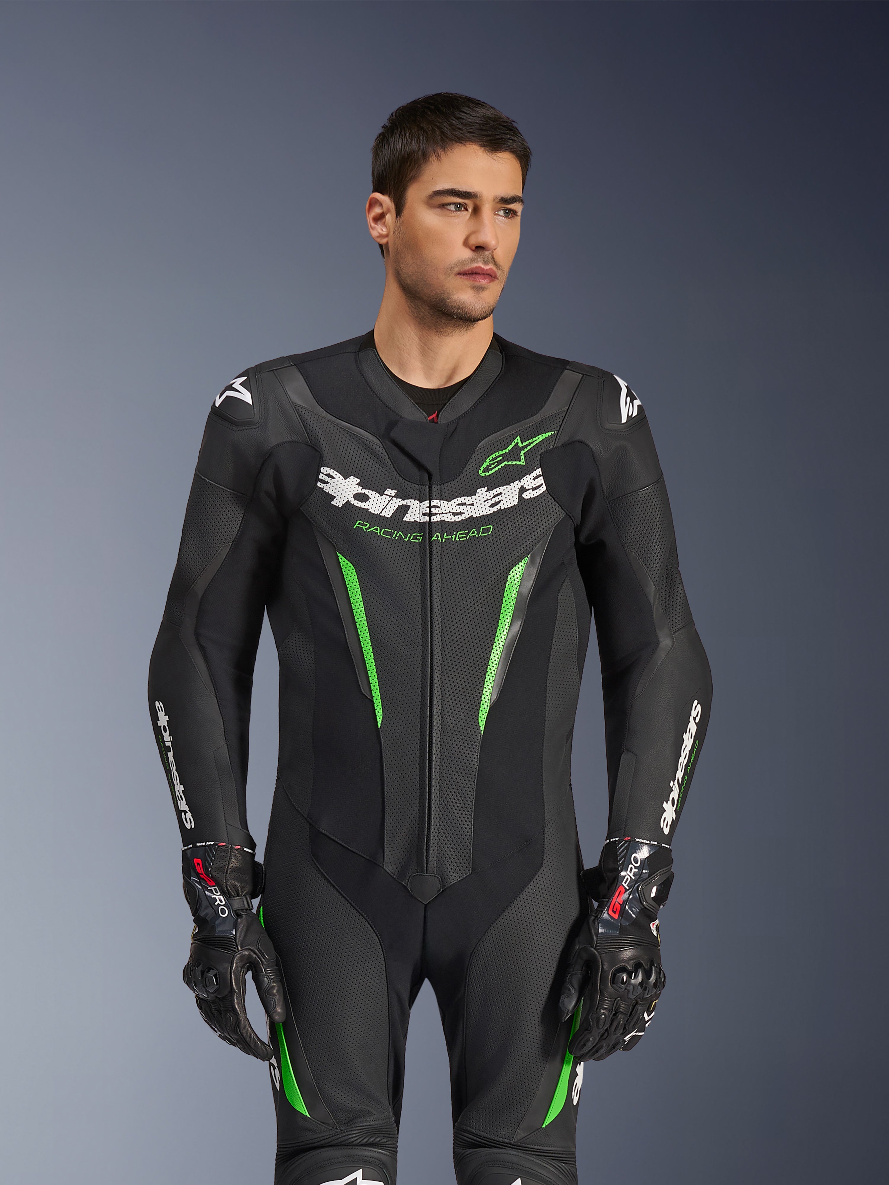 Alpinestars GP Force V2 Leather Suit - 1Piece, czarno-zielony motocyklowy kombinezon wyścigowy prezentowany przez modela, z perforowanymi panelami skórzanymi, wyraźnym białym logo Alpinestars na klatce piersiowej i rękawach oraz zintegrowaną ochroną ramion.