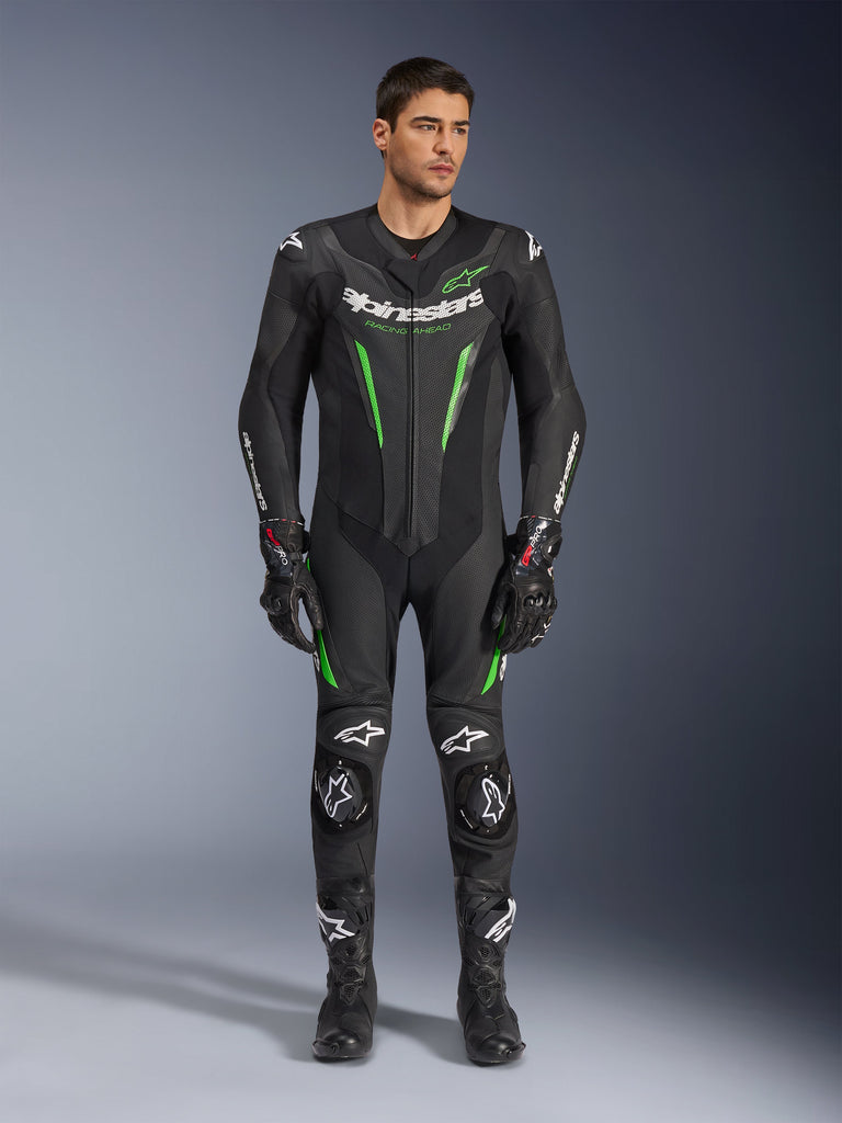Alpinestars GP Force V2 Leather Suit - 1Piece, jednoczęściowy skórzany kombinezon motocyklowy, czarno-zielony, widok z przodu na modela mającego na sobie kombinezon z białym brandingiem na klatce piersiowej i neonowo-zielonymi akcentami, wykonany z perforowanej skóry z zewnętrznymi sliderami ramion, w zestawie z czarnymi rękawicami i butami wyścigowymi