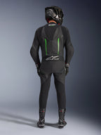 Motocyklista widoczny od tyłu w jednoczęściowym skórzanym kombinezonie Alpinestars GP Force V2 w kolorze czarno-zielonym, czarny kask z włókna węglowego, czarne rękawice wyścigowe i czarne buty, aerodynamiczny garb oraz branding Tech-Air Ready.