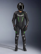 Motocyklista wyścigowy ubrany w jednoczęściowy kombinezon skórzany Alpinestars GP Force V2 w kolorze czarno-zielonym, w zestawie z kaskiem z włókna węglowego i rękawicami wyścigowymi, z perforowanymi panelami skórzanymi i białymi logo Alpinestars, profesjonalny sprzęt do jazdy torowej i sportowej
