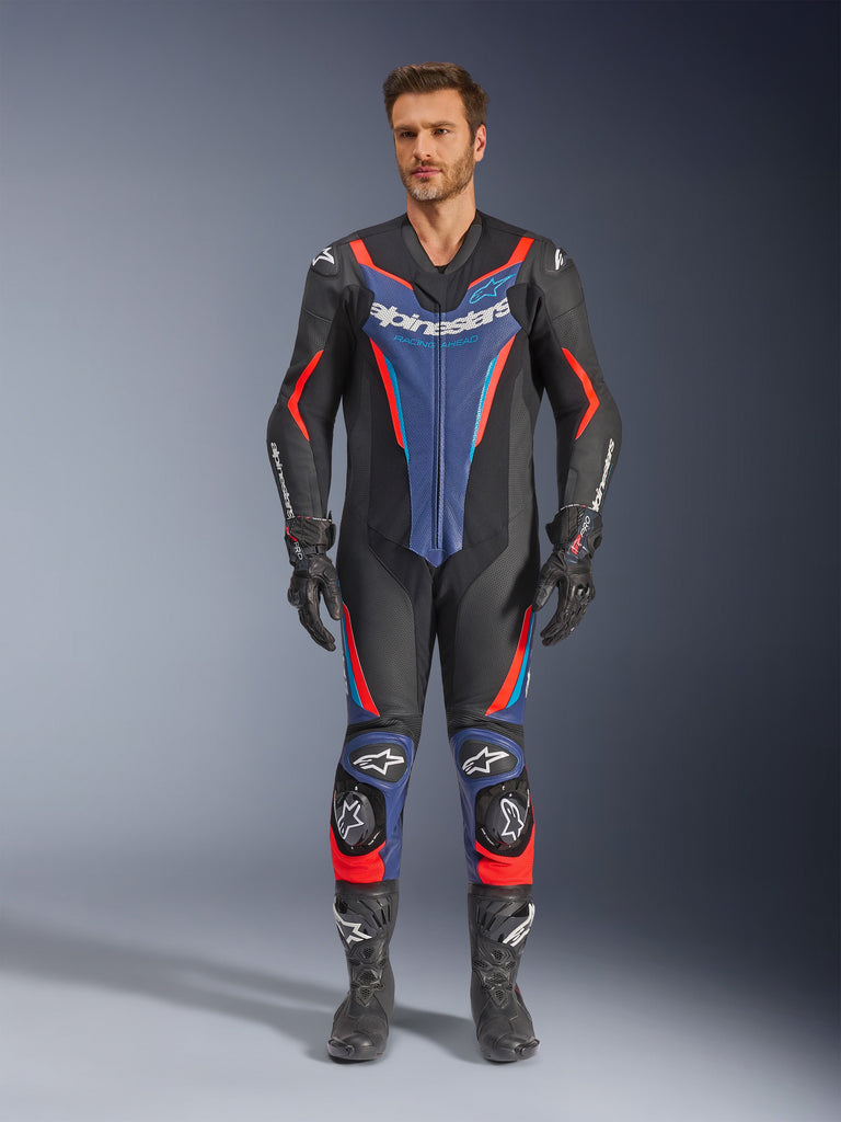 Alpinestars GP Force V2, jednoczęściowy kombinezon wyścigowy ze skóry, męski, czarny z czerwonymi i niebieskimi pasami, z logotypami na klatce piersiowej i kolanach, wzmocnienia na ramionach, łokciach i goleniach, aerodynamiczny krój, czarne rękawice i buty z białymi akcentami
