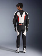 Alpinestars GP Force V2 Leather Suit 1-Piece, motocyklowy kombinezon wyścigowy, biało-czarno-czerwony fluo, widok z tyłu na modela w kombinezonie z butami i rękawicami wyścigowymi, posiada aerodynamiczny garb, harmonijkowe panele elastyczne i oznakowanie Tech-Air Ready