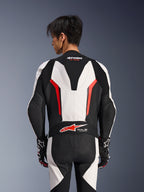 Alpinestars GP Force V2 Leather Suit 1Piece, biało-czarno-czerwony fluo, widok z tyłu na modelu, aerodynamiczny garb, perforowane panele skórzane, logo Tech-Air Ready w dolnej części pleców, profesjonalna odzież wyścigowa z czarno-białymi rękawicami