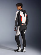 Motocyklista w jednoczęściowym skórzanym kombinezonie Alpinestars GP Force V2, biało-czarno-czerwony (fluo), widok z tyłu ukazujący aerodynamiczny garb i perforowane panele skórzane, pasujące buty i rękawice wyścigowe, do jazdy torowej i sportowej.