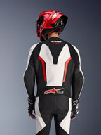 Widok z tyłu jednoczęściowego kombinezonu skórzanego Alpinestars GP Force V2 w kolorystyce biało-czarno-czerwonej (Red Fluo), z czerwonym kaskiem wyścigowym, logo Tech-Air Ready na dole pleców, perforowanymi panelami skórzanymi i harmonijkowymi strefami rozciągliwymi.
