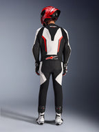 Alpinestars GP Force V2 Leather Suit - 1Piece, biało-czarno-czerwony fluo, widok z tyłu podkreślający aerodynamiczny garb i branding Tech-Air Ready, noszony z czerwonym kaskiem wyścigowym i biało-czarnymi butami, skórzany kombinezon torowy do jazdy wyczynowej.