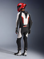 Alpinestars GP Force V2 Leather Suit - 1Piece, biało-czarno-czerwony fluo, widok z tyłu motocyklisty w pełnym stroju wyścigowym, w tym czerwony kask, czarno-białe buty i rękawice, podkreślający aerodynamiczny garb i ergonomiczne panele elastyczne.