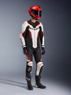 Alpinestars GP Force V2 Leather Suit 1-Piece, biało-czarno-czerwony fluo, zdjęcie studyjne całej sylwetki motocyklisty w pełnym stroju wyścigowym, czerwony kask, czarne rękawice i buty, aerodynamiczna konstrukcja ze skóry bydlęcej, wyraźne logo, zintegrowane slidery kolan.
