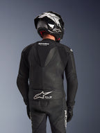Dwuczęściowy skórzany kombinezon Alpinestars GP Force V2, czarny, widok z tyłu na motocyklistę prezentujący aerodynamiczny garb, perforowane panele skórzane oraz harmonijkowe strefy elastyczne na ramionach, z logo Tech-Air Ready w dolnej części pleców, noszony z pasującym kaskiem wyścigowym i rękawicami.