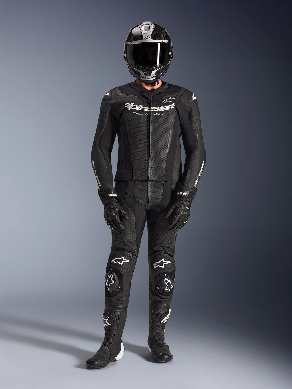 Dwuczęściowy skórzany kombinezon Alpinestars GP Force V2, czarny, kompletny motocyklowy strój wyścigowy obejmujący kask, rękawice i buty, z perforowanymi panelami skórzanymi i białymi logo Alpinestars na klatce piersiowej oraz kolanach, przeznaczony do wyczynowej jazdy na torze