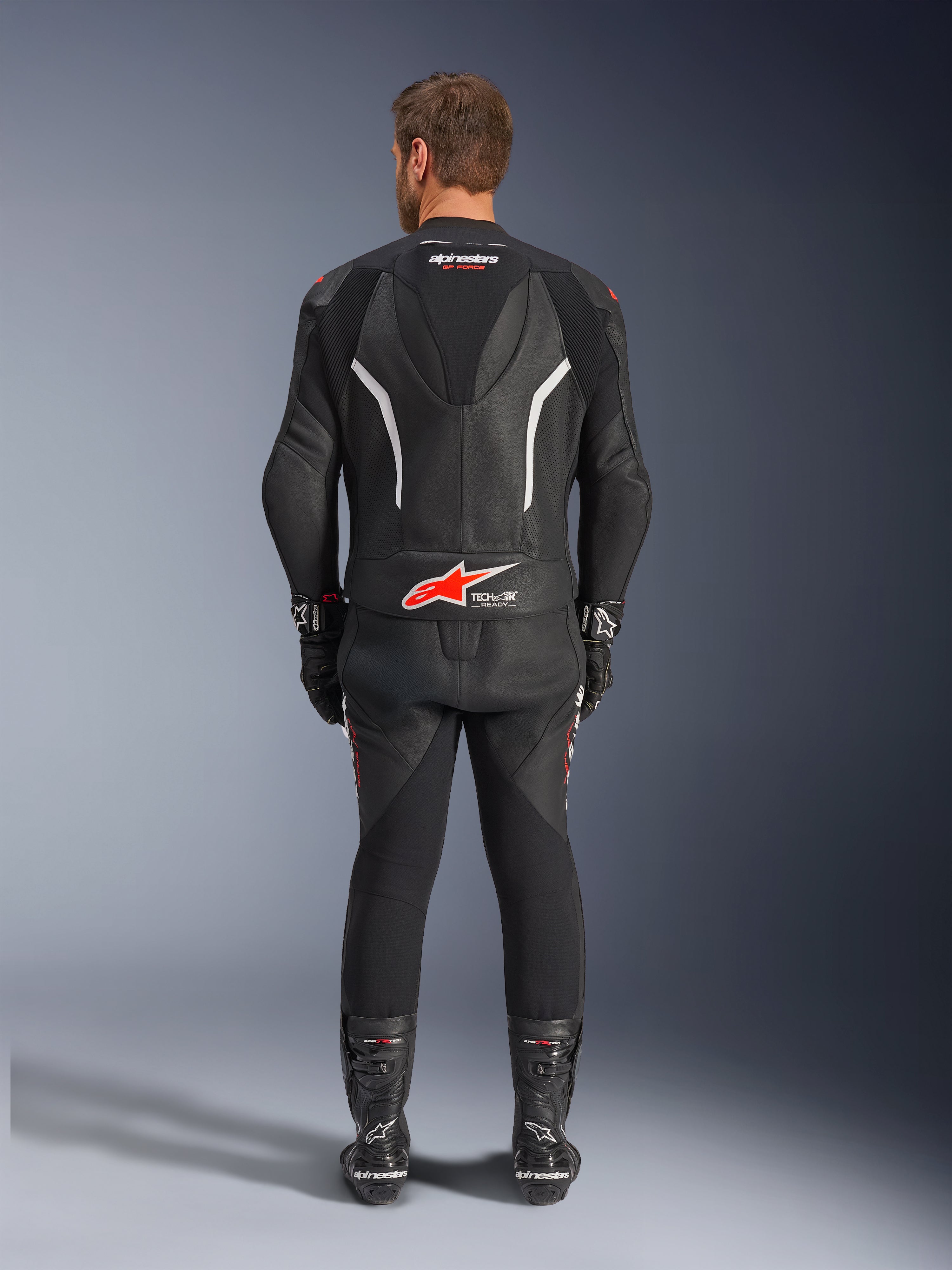 Alpinestars GP Force V2 2-Piece Leather Suit, dwuczęściowy skórzany kombinezon motocyklowy, widok od tyłu, czarny z białymi i czerwonymi akcentami, logo Alpinestars i Tech-Air Ready na plecach, czarne rękawice i buty wyścigowe
