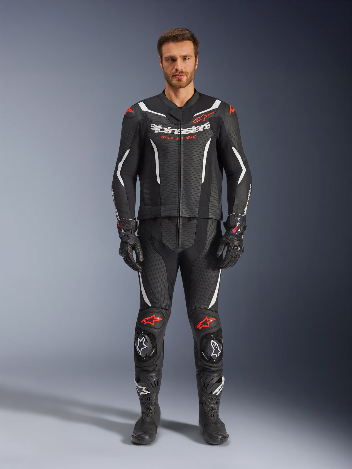 Alpinestars GP Force V2 2-Piece Leather Suit, Motorcycle Racing Suit, Black White and Red Fluo, worn by a model with matching black gloves and boots, featuring perforated leather panels, white and red fluo accents, and a sleek aerodynamic design for track and sport riding