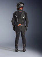 Motocyklista widziany od tyłu w dwuczęściowym skórzanym kombinezonie Alpinestars GP Force V2, czarny z białymi i czerwonymi akcentami fluo, z aerodynamicznym garbem i logo Tech-Air Ready, czarny kask wyścigowy, rękawice i buty.