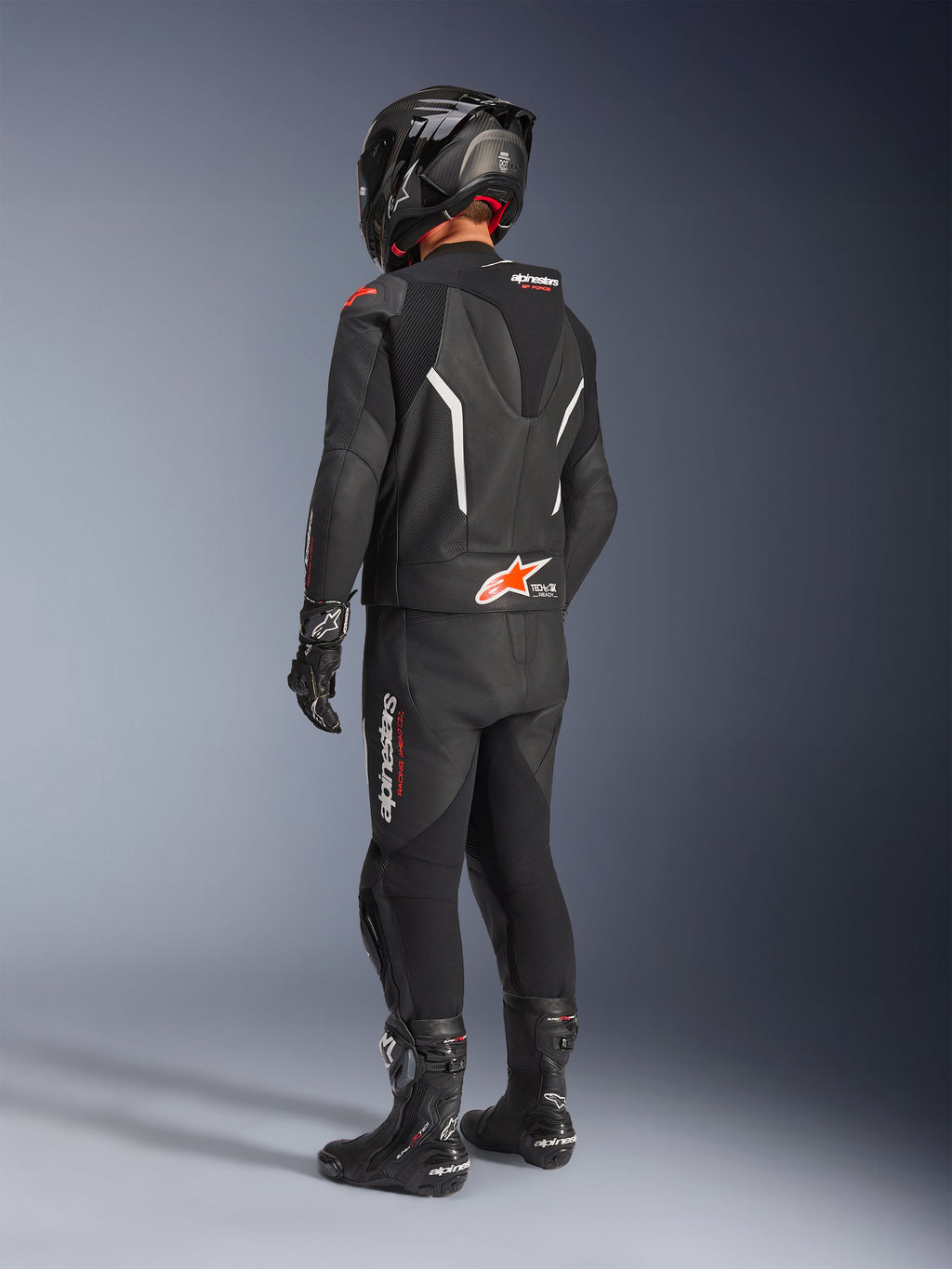 Alpinestars GP Force V2 Leather Suit - 2Piece, czarny dwuczęściowy skórzany kombinezon motocyklowy widziany z tyłu, zestawiony z pasującym czarnym kaskiem, rękawicami i butami, białe i czerwone akcenty, aerodynamiczny garb z logo Alpinestars, profesjonalna odzież wyścigowa i sportowa.