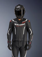 Alpinestars GP Force V2 2-Piece Leather Suit, czarno-biało-czerwony fluo, noszony przez motocyklistę w kasku integralnym z włókna węglowego i czarnych rękawicach wyścigowych, z perforowanymi panelami skórzanymi i logo Alpinestars na klatce piersiowej.