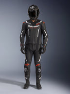 Alpinestars GP Force V2 Leather Suit 2-Piece, dwuczęściowy skórzany kombinezon motocyklowy, czarno-biały z akcentami Red Fluo, białe logo Alpinestars na klatce piersiowej, czerwone detale na ramionach i kolanach, w zestawie z czarnym kaskiem integralnym, czarnymi rękawicami i czarnymi butami.