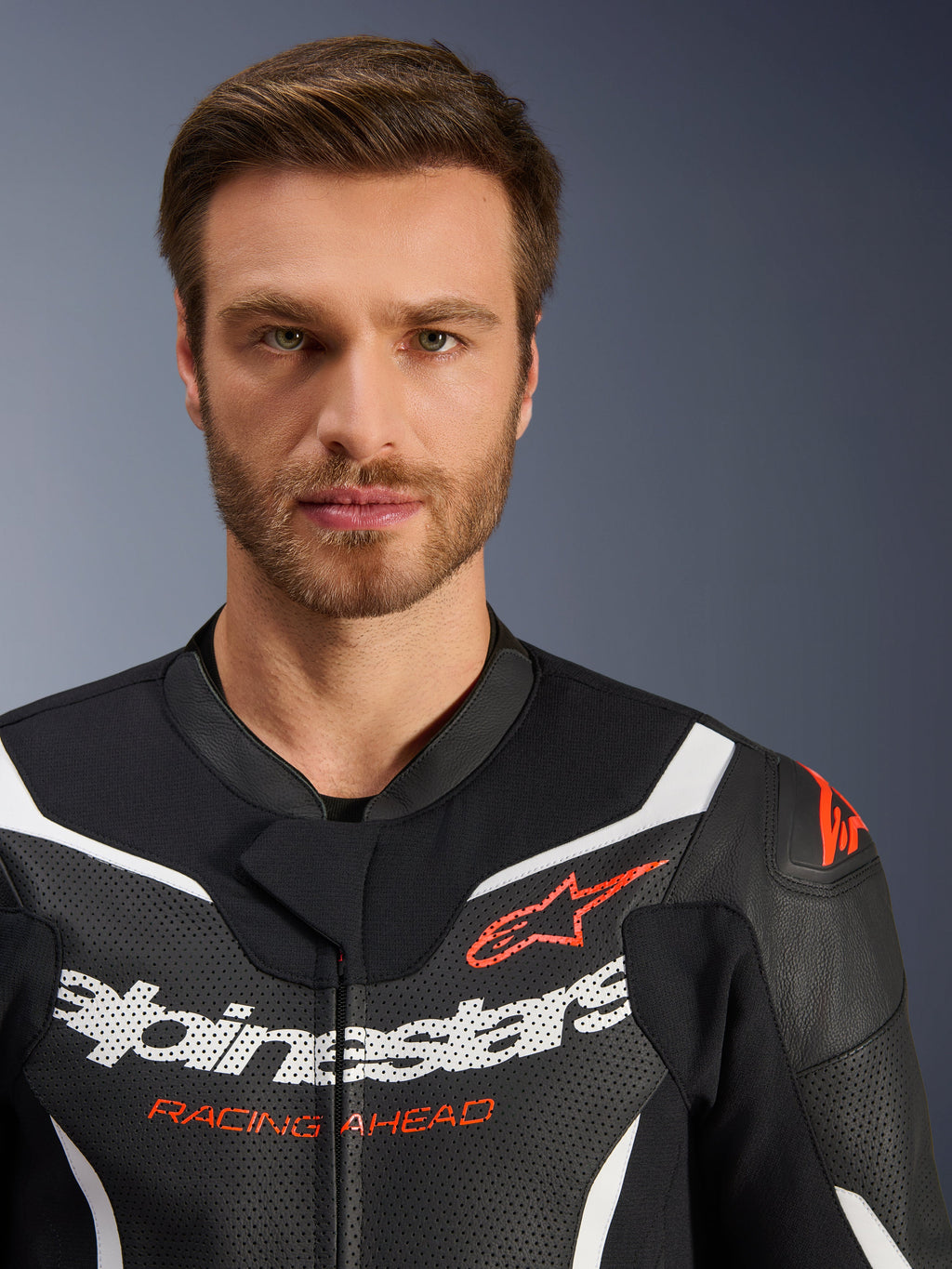 Kurtka dwuczęściowego kombinezonu skórzanego Alpinestars GP Force V2, czarno-biało-czerwona fluo, zbliżenie na perforowaną skórę, białe logo Alpinestars i czerwony napis „RACING AHEAD”, wyczynowa odzież motocyklowa