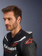Alpinestars GP Force V2 Leather Suit 2-Piece, zbliżenie na kurtkę noszoną przez modela, czarno-biało-czerwony fluo, perforowana skóra, czerwone logo gwiazdy na ramieniu, aerodynamiczny garb i branding na klatce piersiowej, profesjonalna odzież motocyklowa