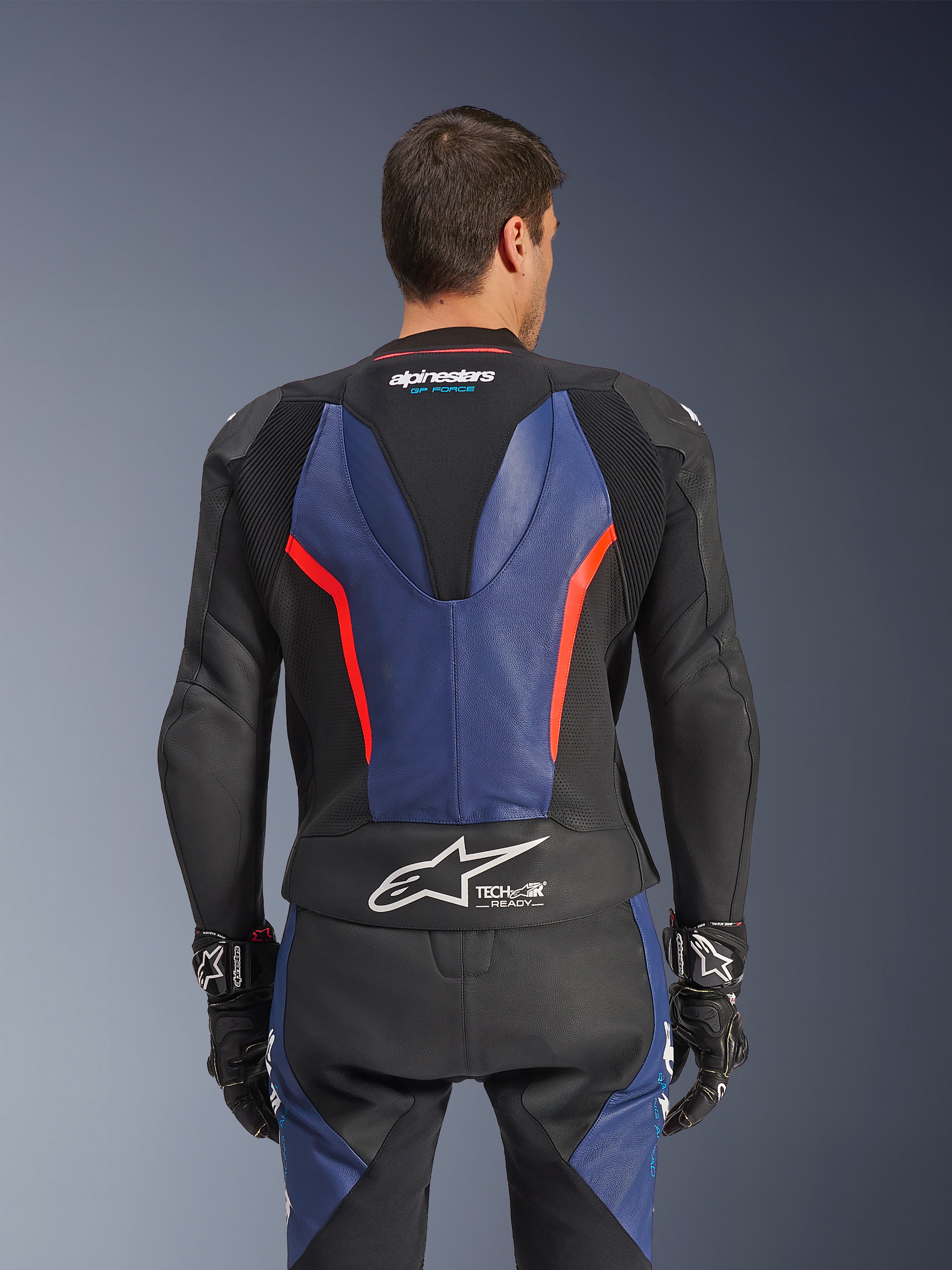 Alpinestars GP Force V2 Leather Suit 2-Piece, dwuczęściowy kombinezon skórzany, widok z tyłu, czarny z niebieskimi i czerwonymi akcentami fluo, perforowana konstrukcja skórzana, logo Tech-Air Ready w pasie, ergonomiczne panele elastyczne dla wydajności wyścigowej.