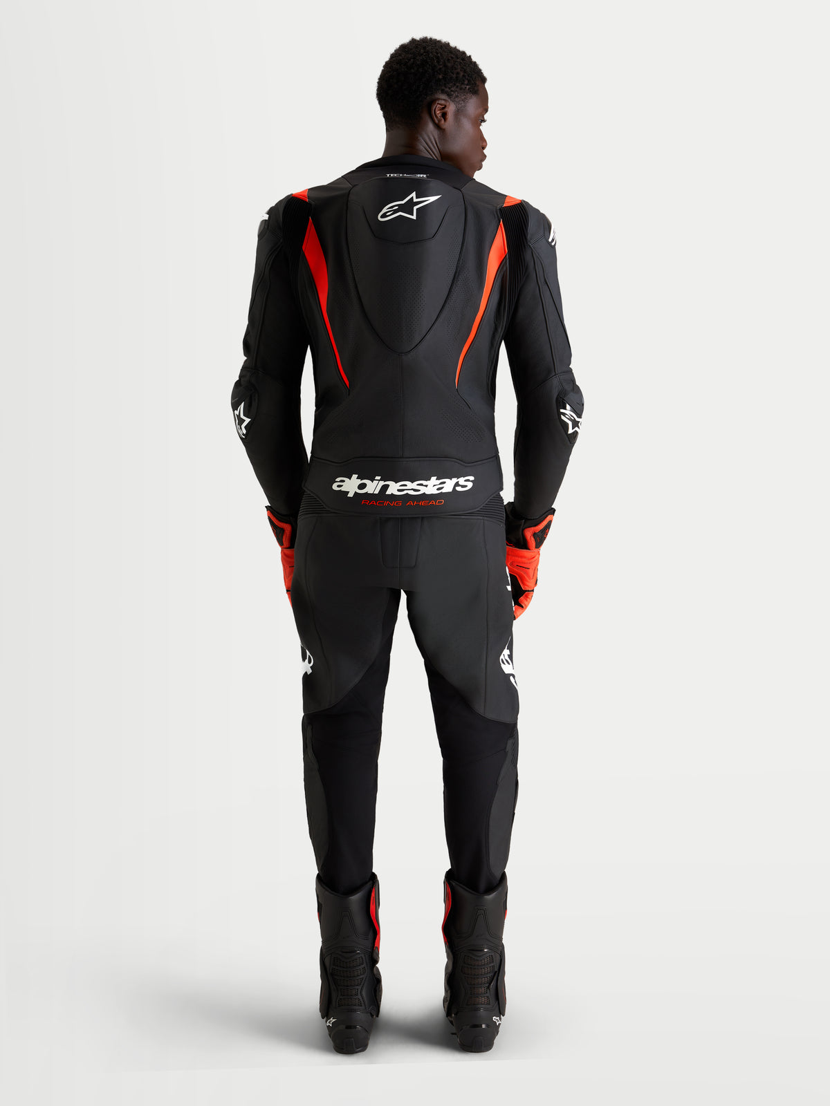 Alpinestars Missile V3 Skórzany Kombinezon 2 Pc, męski motocyklowy skórzany kombinezon wyścigowy, czarny i czerwony fluo, z aerodynamicznym garbkiem i certyfikowaną ochroną AAA, widok z tyłu na zawodnika w kombinezonie