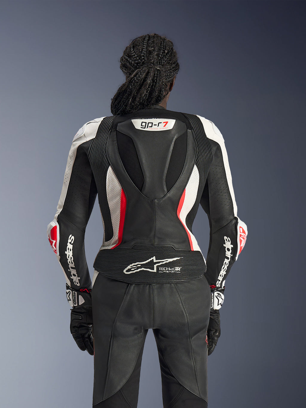 Widok z tyłu dwuczęściowego skórzanego kombinezonu Alpinestars Stella GP-R7 w kolorze Black White Red Fluo, z aerodynamicznym garbem wyścigowym z brandingiem GP-R7, perforowanymi panelami skórzanymi, harmonijkowymi strefami elastycznymi i logo Tech-Air® Ready w dolnej części pleców.