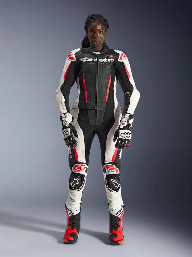 Modelka w dwuczęściowym skórzanym kombinezonie Alpinestars Stella GP-R7 w kolorze czarnym, białym i czerwonym fluo, w komplecie z dopasowanymi rękawicami i butami wyścigowymi, z ochronnymi protektorami i perforowanymi panelami skórzanymi, profesjonalna odzież motocyklowa