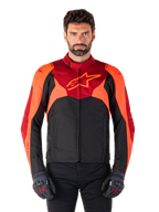 Alpinestars T-Jaws V4 Waterproof Jacket, sportowa tekstylna kurtka motocyklowa, czarna z akcentami czerwonymi fluo i ciemnoczerwonymi, noszona przez modela z dopasowanymi rękawicami, techniczna odzież motocyklowa z wyraźnym logo gwiazdy na piersi