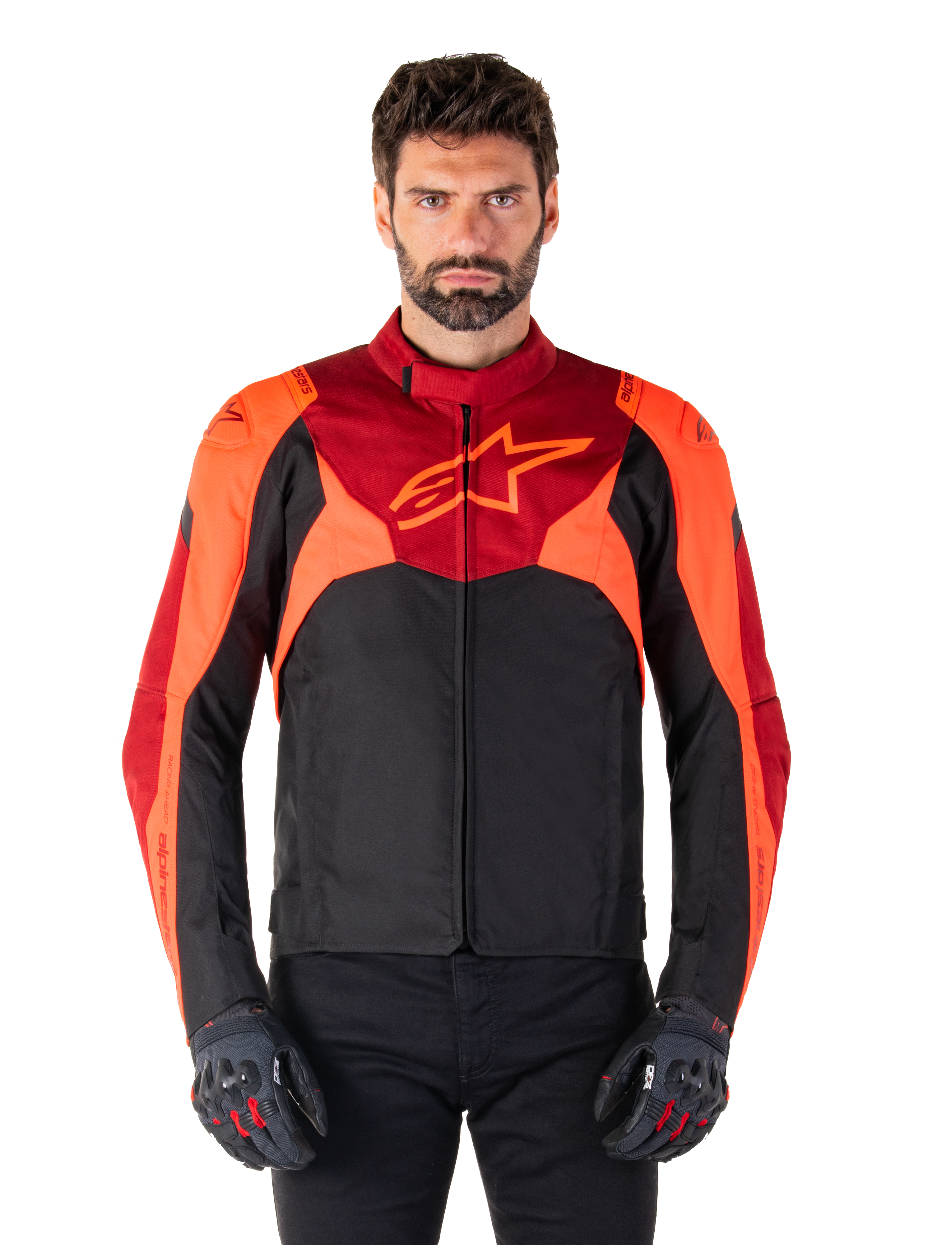 Alpinestars T-Jaws V4 Waterproof Jacket, sportowa tekstylna kurtka motocyklowa, czarna z akcentami czerwonymi fluo i ciemnoczerwonymi, noszona przez modela z dopasowanymi rękawicami, techniczna odzież motocyklowa z wyraźnym logo gwiazdy na piersi